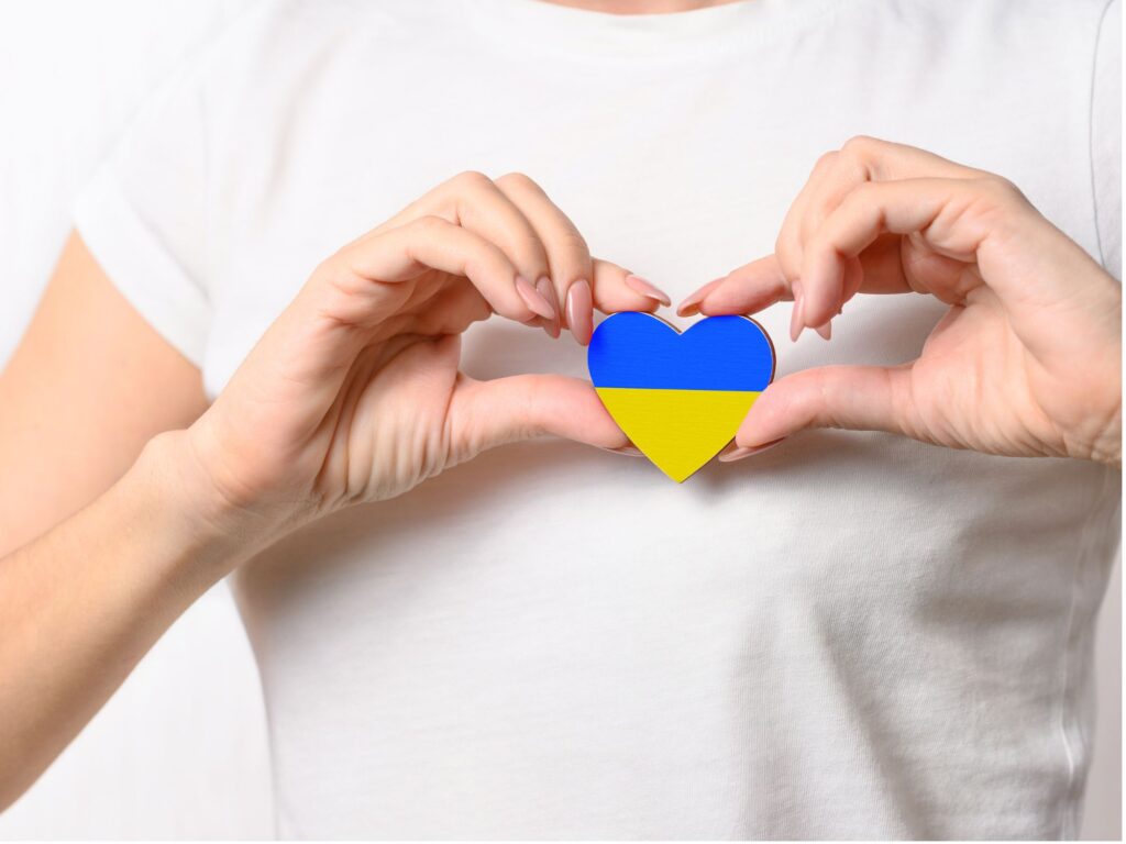 A woman in a white t-shirt holding a yellow and blue heart that resembles the Ukrainian flag