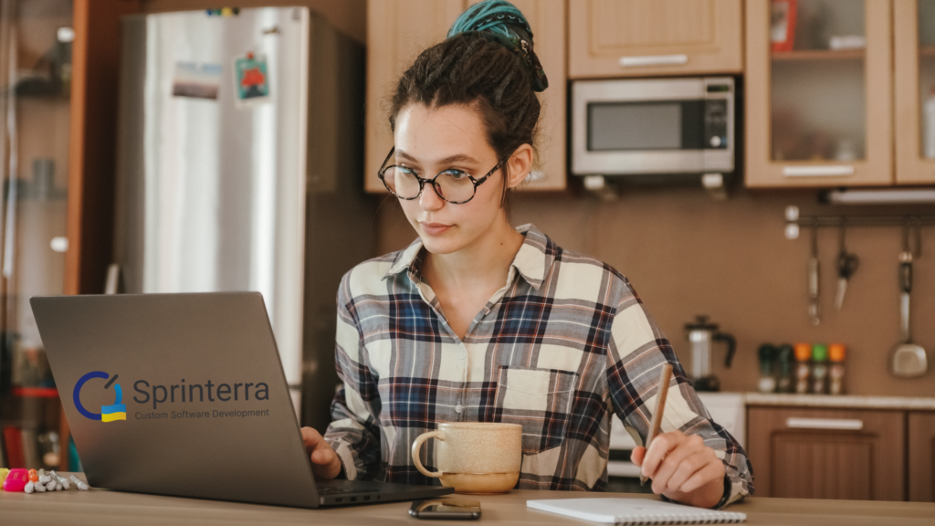 A girl working on a laptop with Sprinterra logo on the computer, kitchen on the background